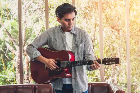 Young guitar player holding his guitar at home. Music and song concept.の写真素材