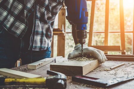 Carpenter working on wood craft at workshop to produce construction material or wooden furniture. The young Asian carpenter use professional tools for crafting. DIY maker and carpentry work concept.の写真素材