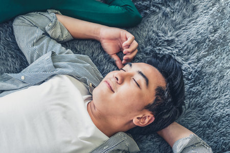 Happy Asian couple lying together on carpet at living room floor. Love relationship and lifestyle concept.の写真素材