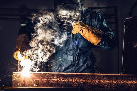 Metal welder working with arc welding machine to weld steel at factory while wearing safety equipment. Metalwork manufacturing and construction maintenance service by manual skill labor concept.の写真素材