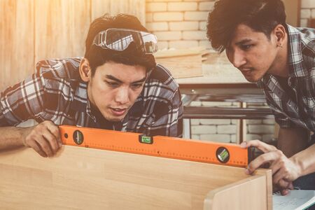 Carpenter working on wood craft at workshop to produce construction material or wooden furniture. The young Asian carpenter use professional tools for crafting. DIY maker and carpentry work concept.の写真素材