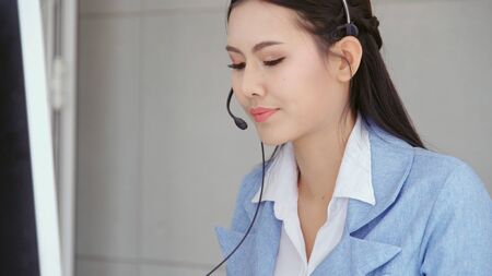 Customer support agent or call center with headset works on desktop computer while supporting the customer on phone call. Operator service business representative concept.の写真素材