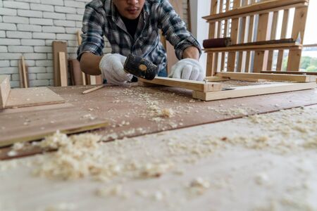 Carpenter working on wood craft at workshop to produce construction material or wooden furniture. The young Asian carpenter use professional tools for crafting. DIY maker and carpentry work concept.の写真素材
