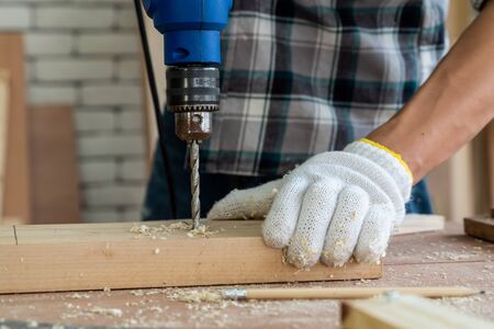 Carpenter working on wood craft at workshop to produce construction material or wooden furniture. The young Asian carpenter use professional tools for crafting. DIY maker and carpentry work concept.の写真素材