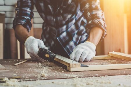 Carpenter working on wood craft at workshop to produce construction material or wooden furniture. The young Asian carpenter use professional tools for crafting. DIY maker and carpentry work concept.の写真素材