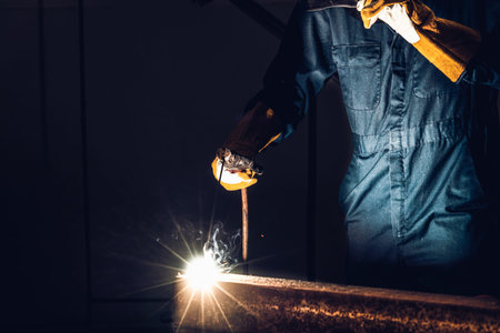 Metal welder working with arc welding machine to weld steel at factory while wearing safety...