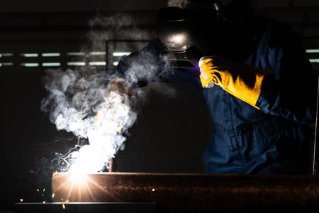 Metal welder working with arc welding machine to weld steel at factory while wearing safety...