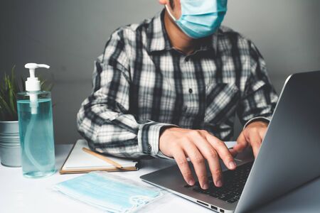 Coronavirus disease or COVID-19 protection concept - Young man work in office room at home with protective and cleaning equipment to protect against corona virus while using laptop computer at desk.の写真素材