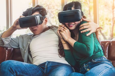 Happy couple watching video in virtual reality VR headset in living room at home. Multimedia movie and entertainment concept.の写真素材