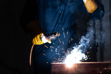 Metal welder working with arc welding machine to weld steel at factory while wearing safety...