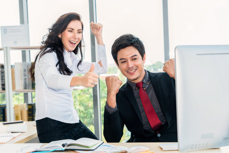 Two happy business people celebrate at office meeting room. Successful businessman congratulate project success with colleague at modern workplace while having conversation on financial data report.の写真素材