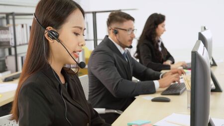 Business people wearing headset working in office to support remote customer or colleague. Call center, telemarketing, customer support agent provide service on telephone video conference call.の写真素材