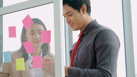 Business people work on project planning board in office and having conversation with coworker...