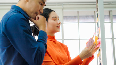 Business people work on project planning board in office and having conversation with coworker friend to analyze project development . They use sticky notes posted on glass wall to make it organized .の写真素材