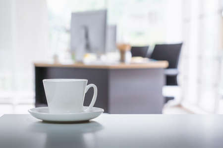 Coffee cup on office table with background of modern office. Coffee break relaxation time.の写真素材