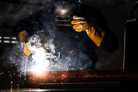 Metal welder working with arc welding machine to weld steel at factory while wearing safety equipment. Metalwork manufacturing and construction maintenance service by manual skill labor concept.の写真素材