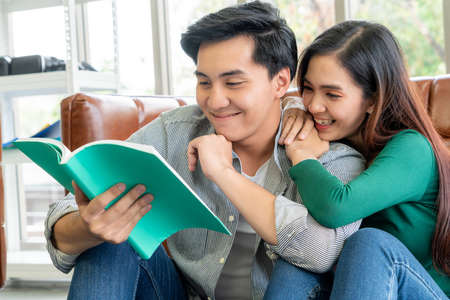 Young Asian couple reading book in living room.の写真素材
