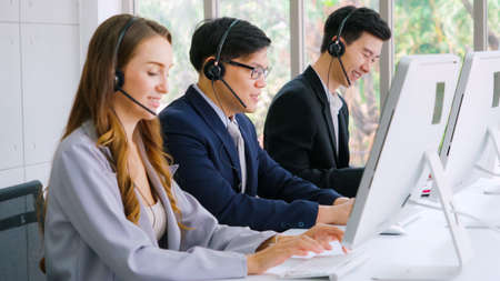 Business people wearing headset working in office to support remote customer or colleague. Call center, telemarketing, customer support agent provide service on telephone video conference call.の写真素材