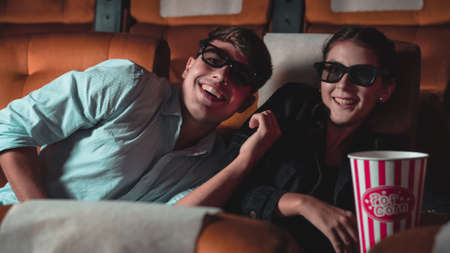 Man and woman in the cinema watching a movie with 3D glasses. with interest looking at the screen, exciting and eating popcornの写真素材