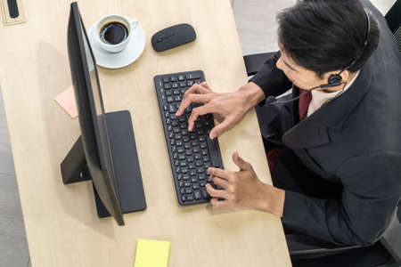Business people wearing headset from top view in office working with computer to support remote customer or colleague. Call center, telemarketing agent service on telephone or video conference call.の写真素材