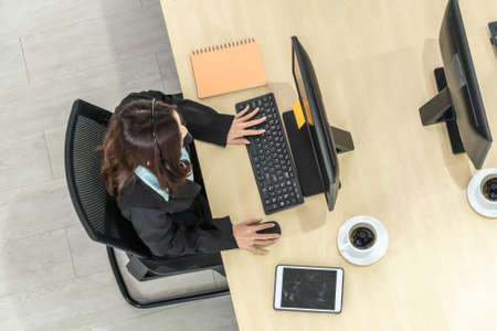 Business people wearing headset from top view in office working with computer to support remote customer or colleague. Call center, telemarketing agent service on telephone or video conference call.の写真素材