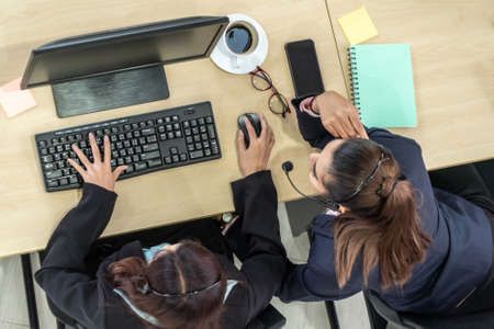 Business people wearing headset from top view in office working with computer to support remote customer or colleague. Call center, telemarketing agent service on telephone or video conference call.の写真素材
