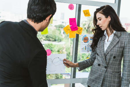 Business people work on project planning board in office and having conversation with coworker friend to analyze project development . They use sticky notes posted on glass wall to make it organized .の写真素材