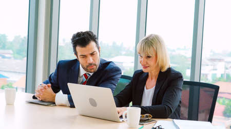 Two business people talk project strategy at office meeting room. Businessman discuss project planning with colleague at modern workplace while having conversation and advice on financial data report.の写真素材