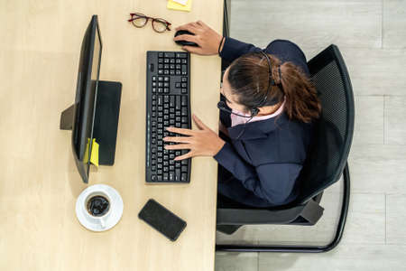 Business people wearing headset from top view in office working with computer to support remote customer or colleague. Call center, telemarketing agent service on telephone or video conference call.の写真素材