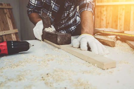 Carpenter working on wood craft at workshop to produce construction material or wooden furniture. The young Asian carpenter use professional tools for crafting. DIY maker and carpentry work concept.の写真素材