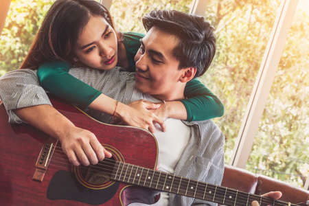 Young Asian Couple Plays Guitar and Sing Song in Living Room at Home Together. Music and Lifestyle concept.の写真素材