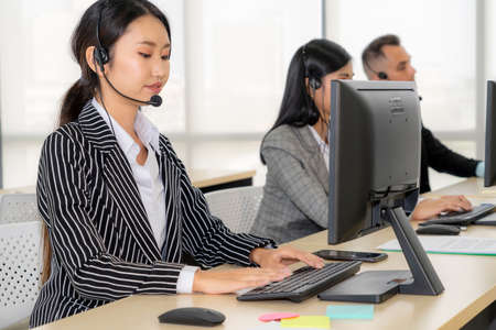 Business people wearing headset working in office to support remote customer or colleague. Call center, telemarketing, customer support agent provide service on telephone video conference call.の写真素材