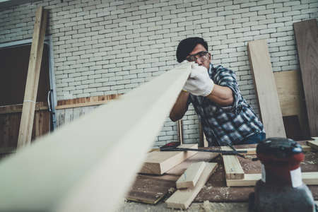 Carpenter working on wood craft at workshop to produce construction material or wooden furniture. The young Asian carpenter use professional tools for crafting. DIY maker and carpentry work concept.の写真素材