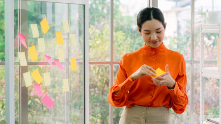 Business people work on project planning board in office and having conversation with coworker friend to analyze project development . They use sticky notes posted on glass wall to make it organized .の写真素材