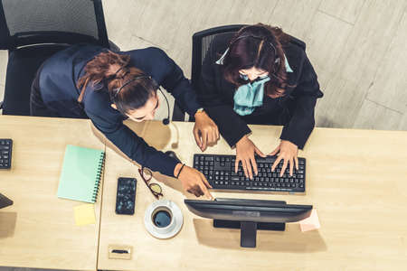 Business people wearing headset from top view in office working with computer to support remote customer or colleague. Call center, telemarketing agent service on telephone or video conference call.の写真素材