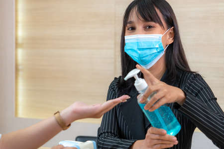 Receptionist and guest wearing face mask at front desk while having conversation in office or hospital . Covid 19 and coronavirus infection protection and protective policy concept .の写真素材