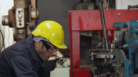 Factory worker talking on portable radio while inspecting machinery parts . Industrial and...