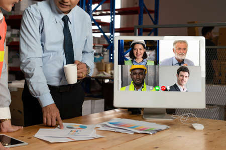 Warehouse staff talking on video call at computer screen in storage warehouse . Online software technology connects people working in logistic factory by virtual conference call on internet network .の写真素材