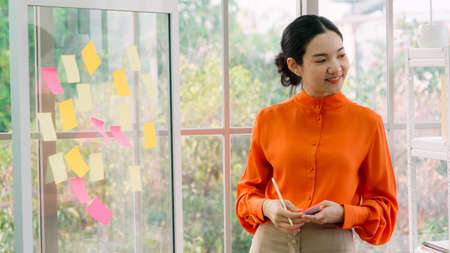 Business people work on project planning board in office and having conversation with coworker friend to analyze project development . They use sticky notes posted on glass wall to make it organized .の写真素材