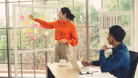 Business people work on project planning board in office and having conversation with coworker friend to analyze project development . They use sticky notes posted on glass wall to make it organized .の写真素材