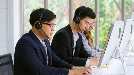 Business people wearing headset working in office to support remote customer or colleague. Call center, telemarketing, customer support agent provide service on telephone video conference call.の写真素材