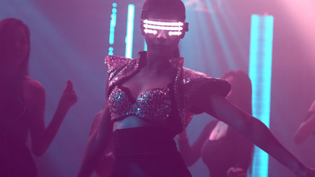 Group of people dance in disco night club to the beat of music from DJ on stage . New year night...