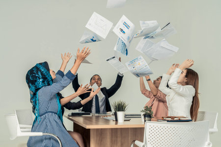 Smiling business people having fun by throwing papers in the air celebrating business success in the...