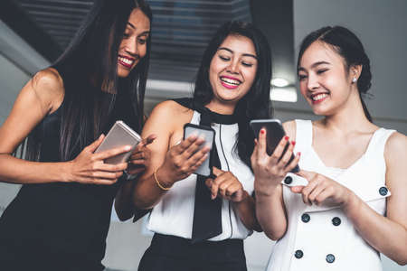 Three women friends having conversation while looking at mobile phone in their hands. Concept of social media, gossip news and online shopping.の写真素材