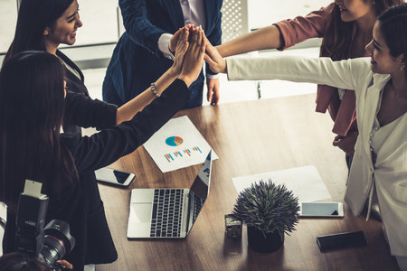 Businesswomen joining hands in group meeting at modern office room showing teamwork, support and...