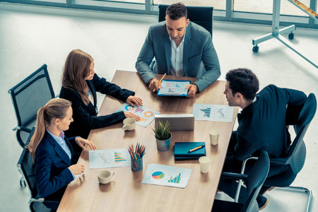 Businessman executive in group meeting discussion with other businessmen and businesswomen in modern office with coffee cups and documents on table. People corporate business working team concept.の写真素材