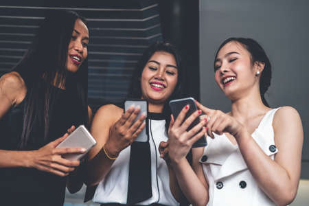 Three women friends having conversation while looking at mobile phone in their hands. Concept of social media, gossip news and online shopping.の写真素材