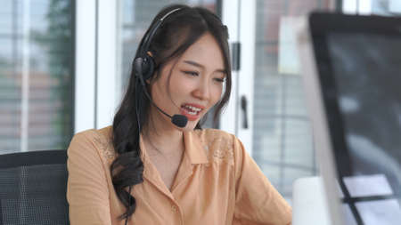 Businesswoman wearing headset working actively in office . Call center, telemarketing, customer support agent provide service on telephone video conference call.の写真素材