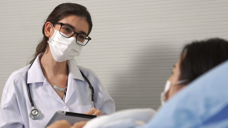 Doctor wearing face mask proficiently talks with patient at hospital ward . Healthcare and medical...