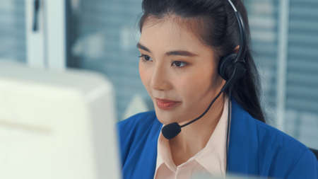 Businesswoman wearing headset working actively in office . Call center, telemarketing, customer support agent provide service on telephone video conference call.の写真素材